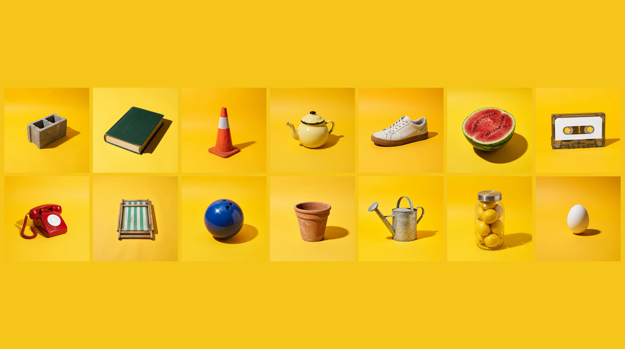 The 14 reference objects laid out on a yellow grid: a cinder block, a hardback book, a traffic cone, an enamel teapot, a white trainer, half a watermelon, a cassette tape, a rotary telephone, a folded deckchair, a bowling ball, a terracotta pot, a watering can, a jar of lemons and a white egg.