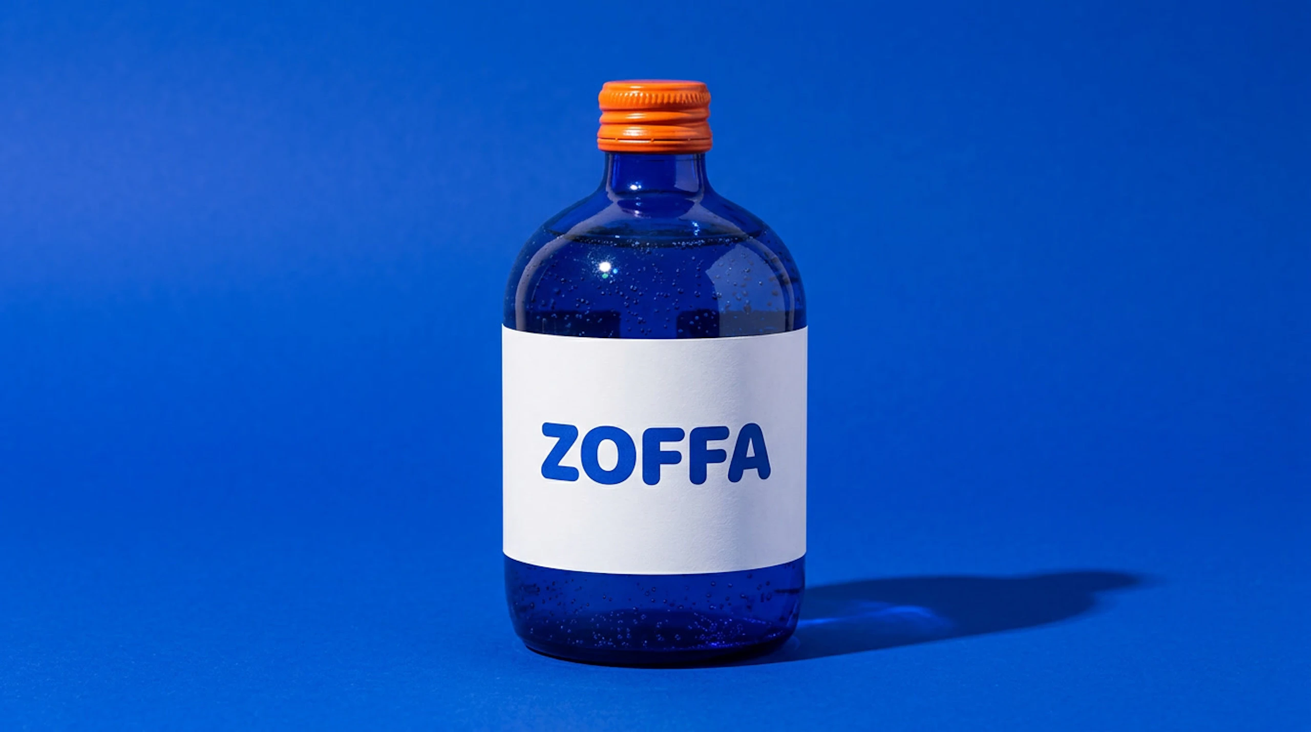 Reference photo of a ZOFFA bottle: cobalt glass, an orange cap and a white label, on a cobalt backdrop.